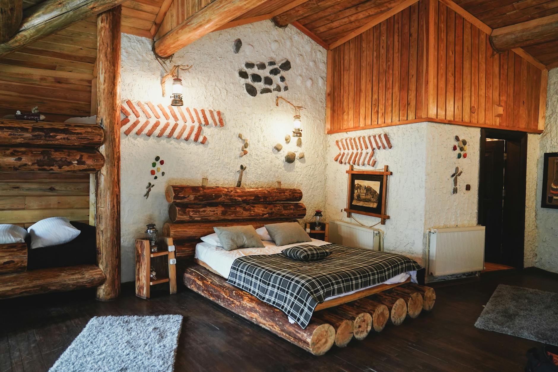 A log-walled bedroom with a plaid blanket, gray pillows, lantern-style wall lights and a shaggy rug