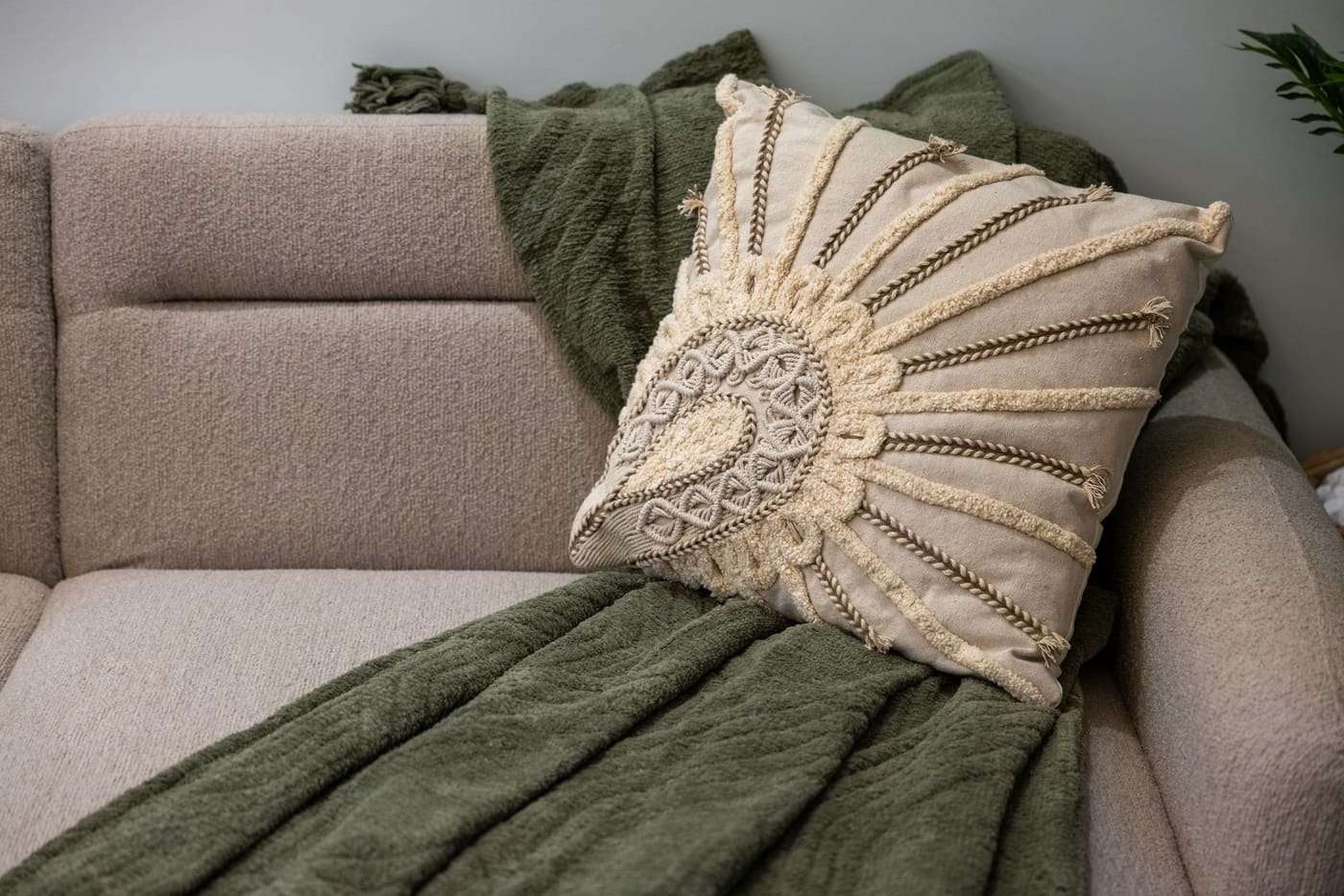 A cream textured pillow and a green knit throw on a beige sofa