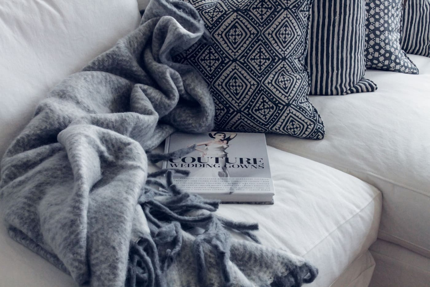 A gray knit throw and patterned pillows on a white sofa with a magazine