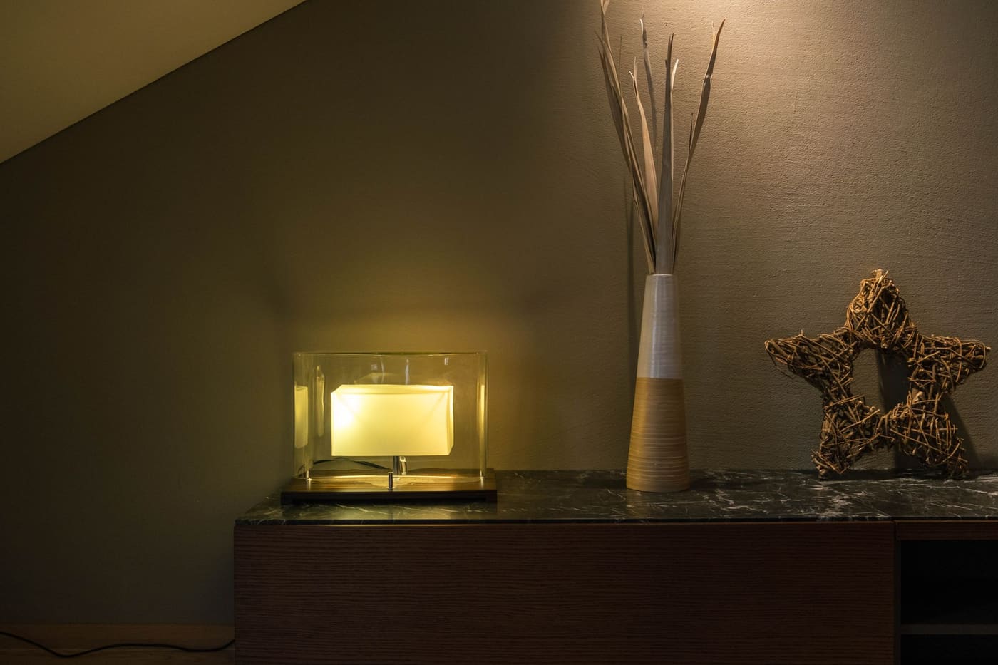 A small glowing lamp on a console next to a tall vase of dry twigs