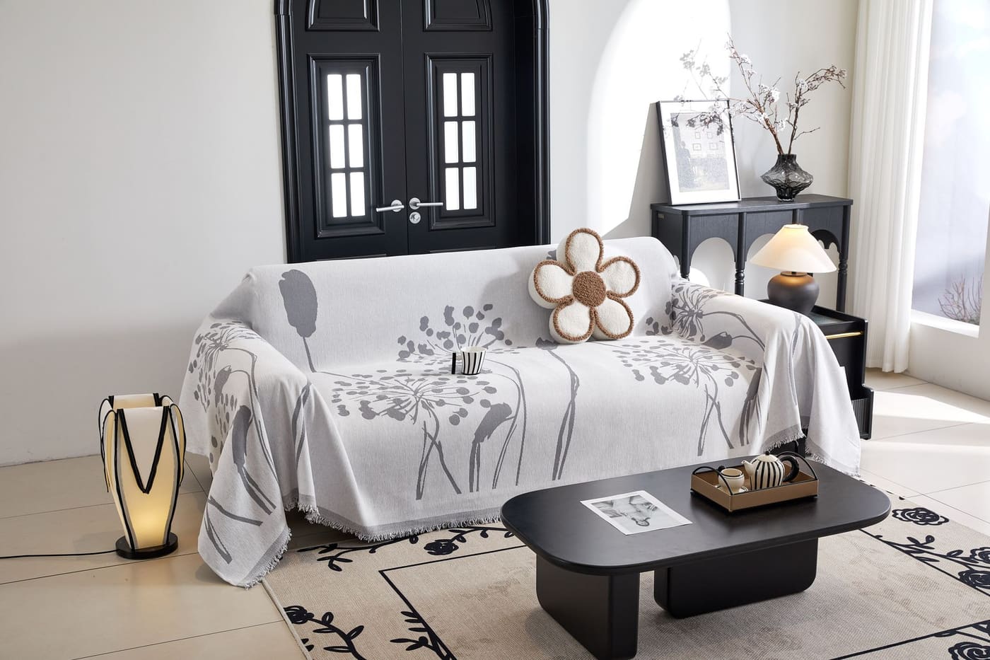 A bright styled living room with a gray patterned sofa cover, black console and coffee table, and a floor lamp