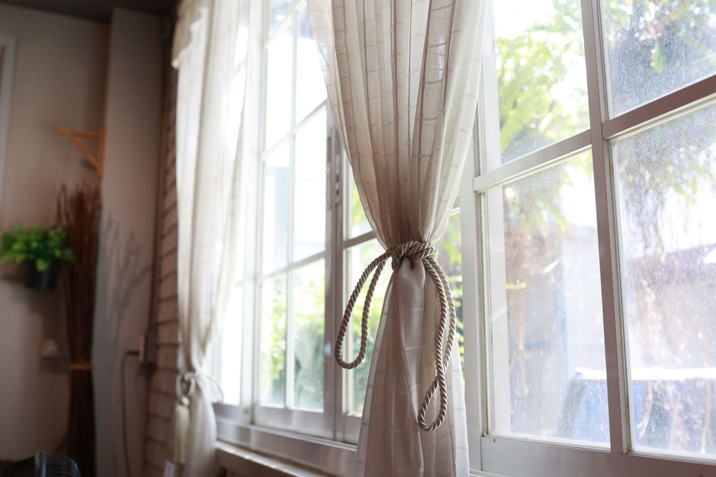 Sheer and linen curtains tied back beside a tall sunlit window
