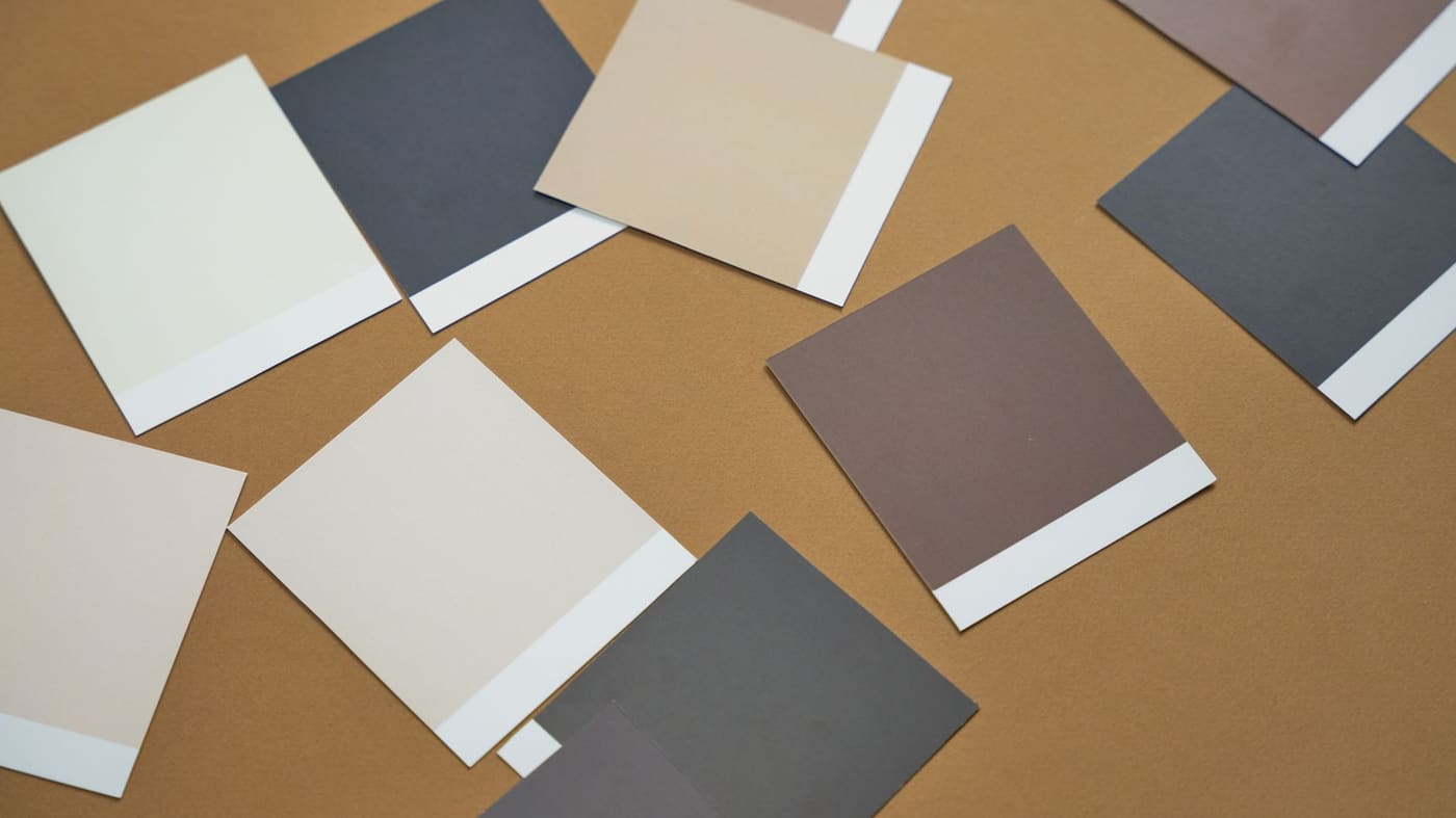 Flat lay of cream, beige, taupe and charcoal paint swatches on a brown surface