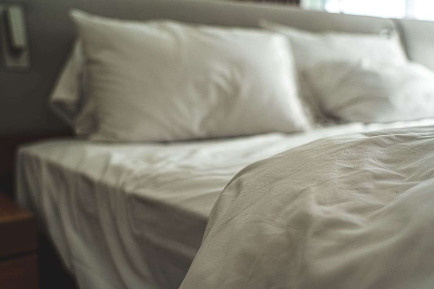 A bed with white linen sheets and soft pillows in gentle light